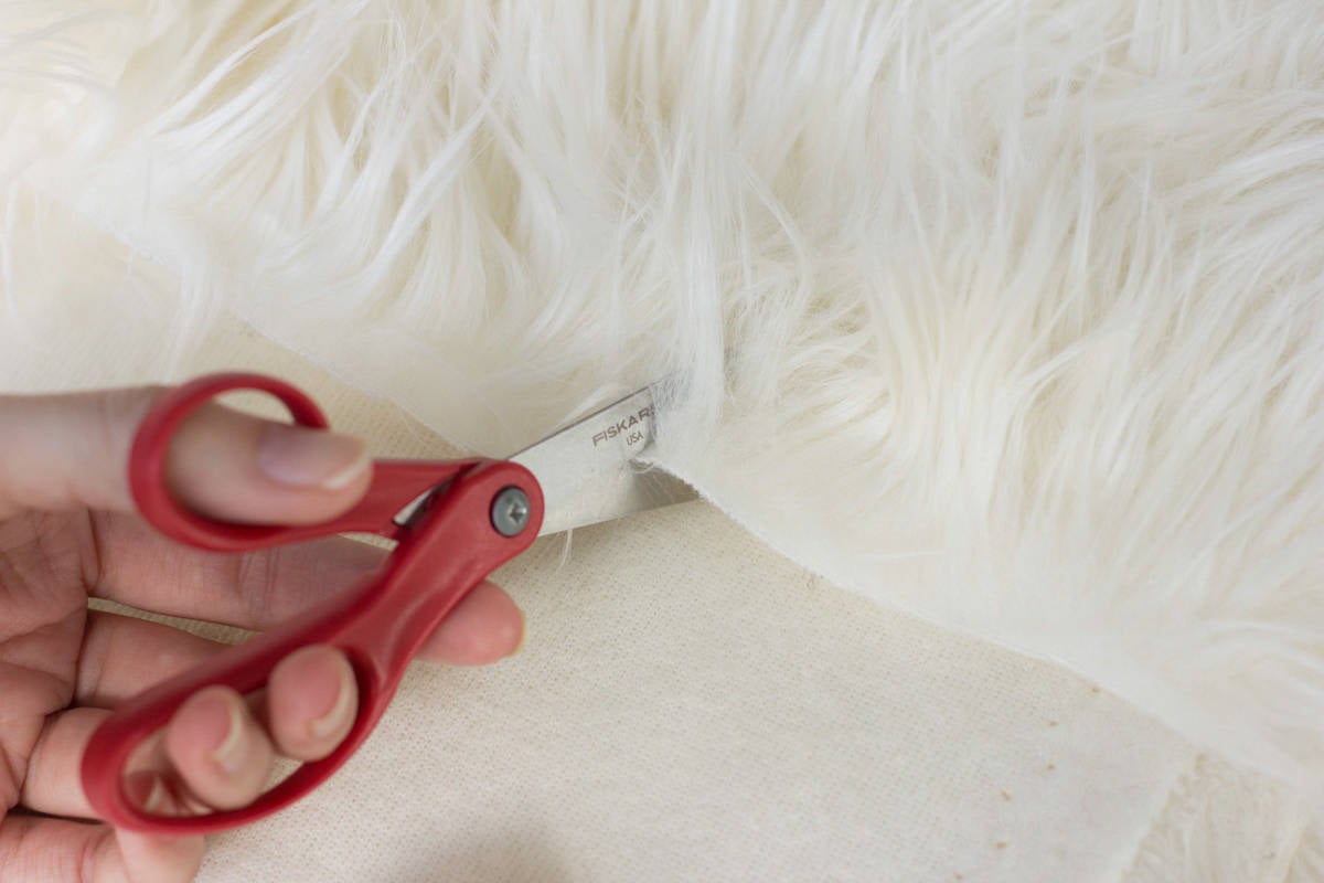 A person adding fur to their crochet or knit project by cutting a piece of white fur.