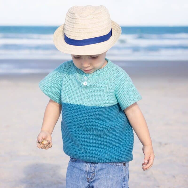 A toddler wearing a crochet summer t-shirt on the beach.