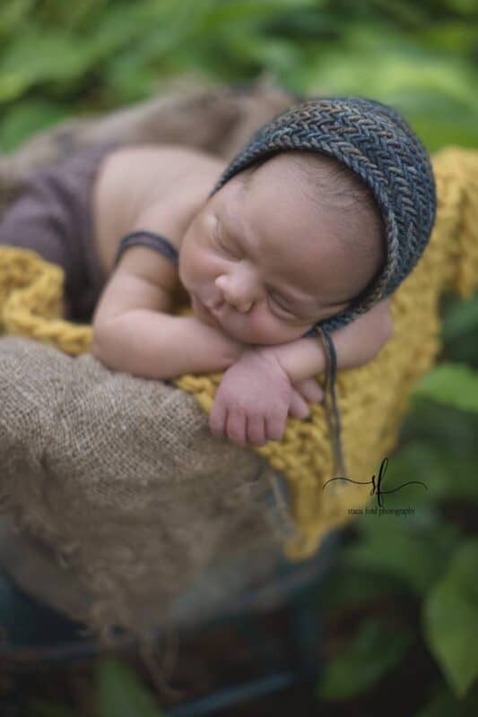 a baby in a basket wearing a knit bonnet with the herringbone knit stitch