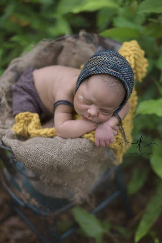 a baby in a basket wearing a knit bonnet with the herringbone knit stitch