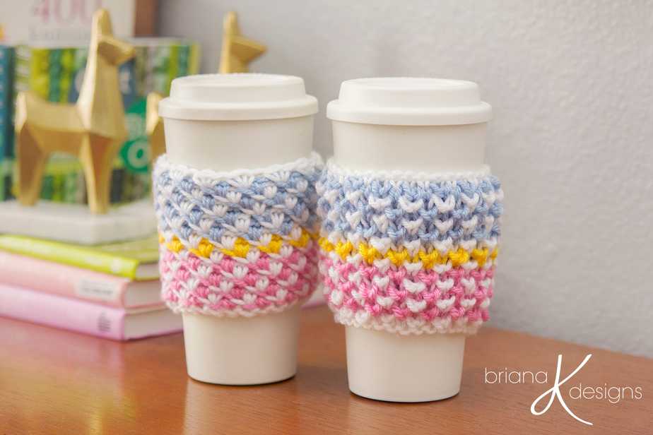 Two crocheted coffee cup cozys on a table in a stylish pattern.