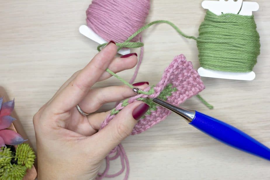 A person is creating colorwork in crochet with a needle and yarn.