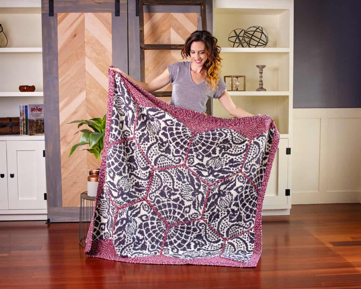 A woman displaying The Gaudi Sidewalk Blanket, a large, patterned quilt, in a home interior.