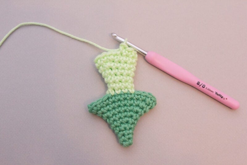 A green crocheted flower with a pink crochet hook, perfect for your Dragon Easter Basket.