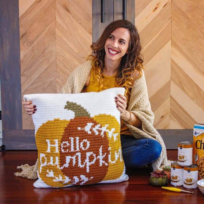 A beginner is sitting on the floor holding a pillow with a hello pumpkin pattern.