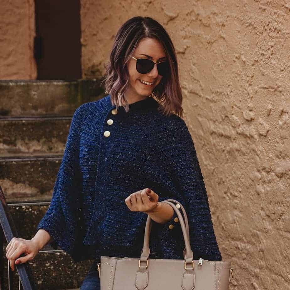 A woman donning a posh blue cape jacket and jeans, clutching a beige tote bag.