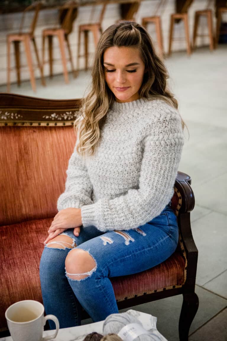 A woman wearing a sweater, sitting on a couch.