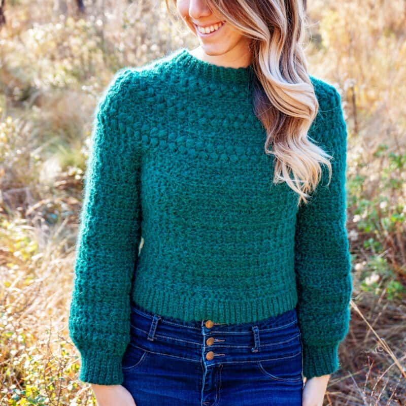 A woman wearing a green macchiato sweater and jeans.