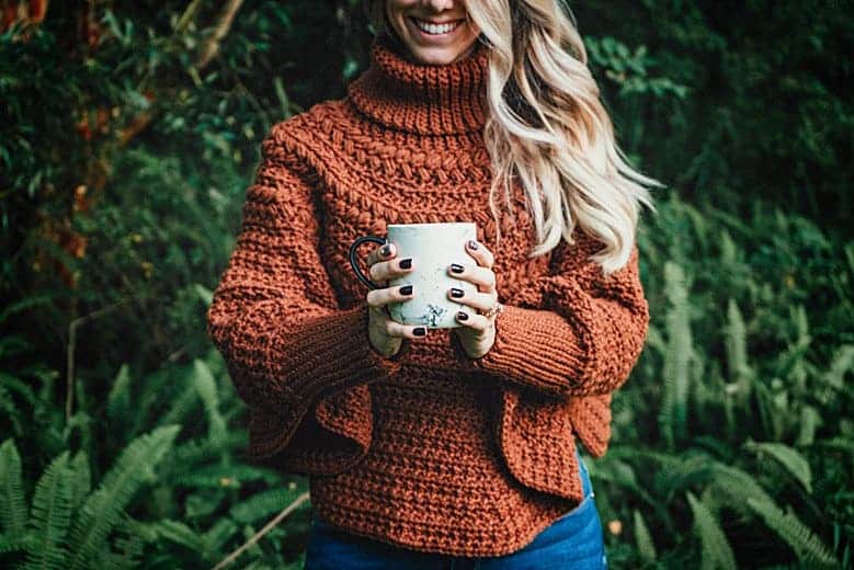 A woman holding a macchiato in the woods.