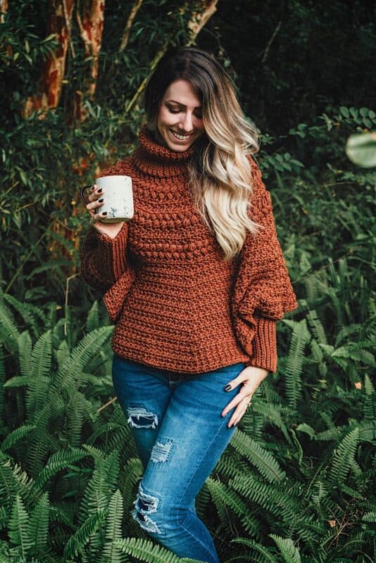 A woman holding a macchiato in a forest.