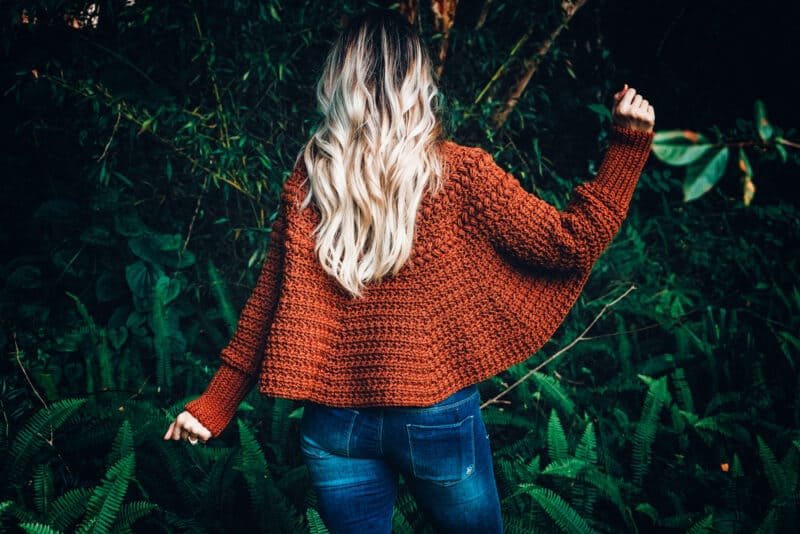 A woman standing in the woods wearing a crocheted Macchiato Poncho.