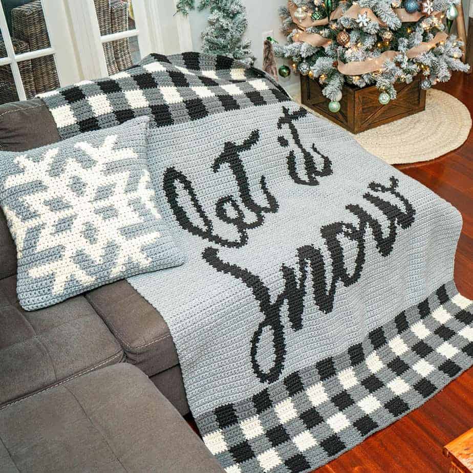A crocheted couch adorned with a "Let It Snow" blanket.