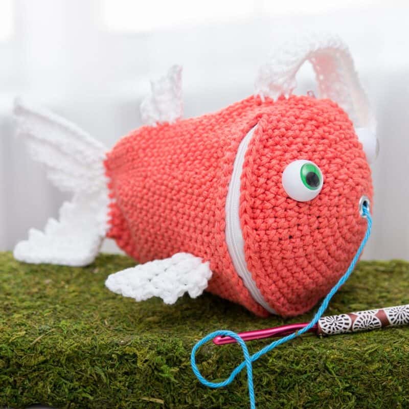 A crocheted fish sitting on top of a mossy surface.