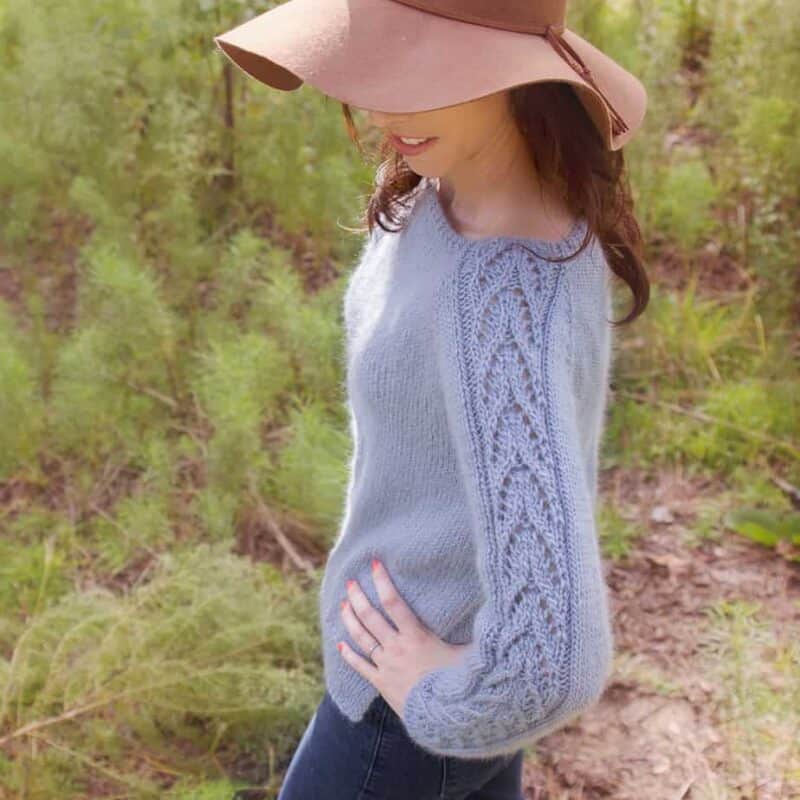 A woman wearing a blue knit sweater in the woods.