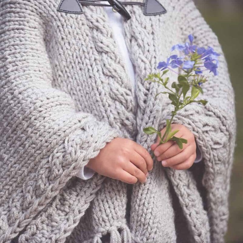 child holding flowers in knit cape