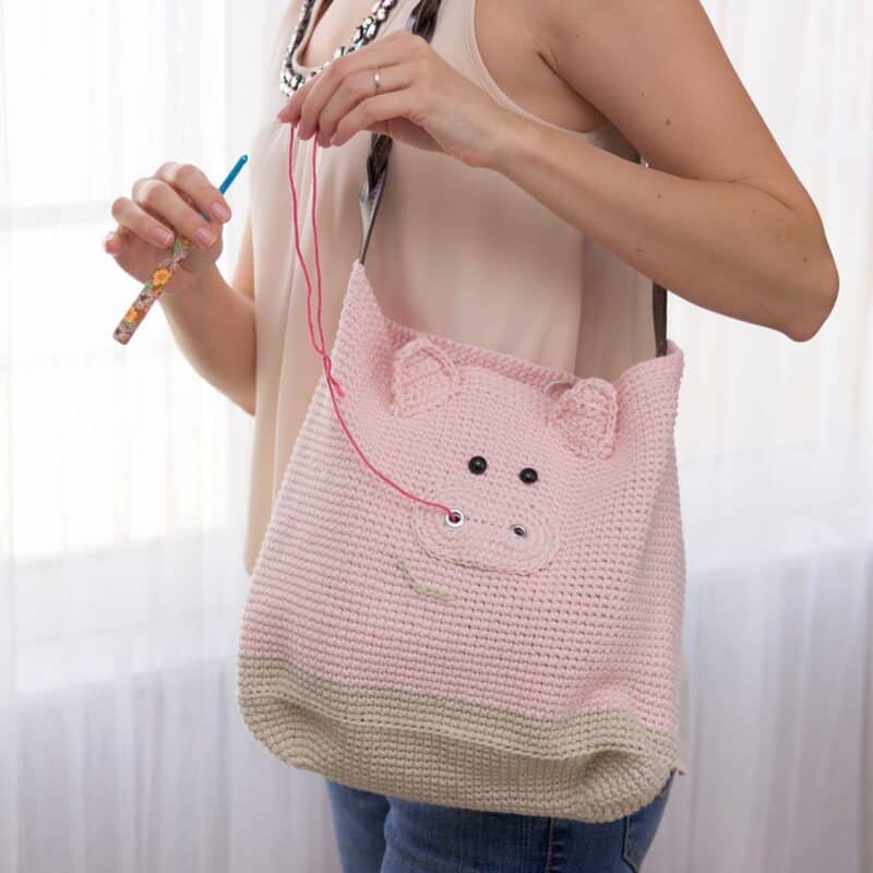 A woman showcasing a pig-shaped crochet bag in pink.