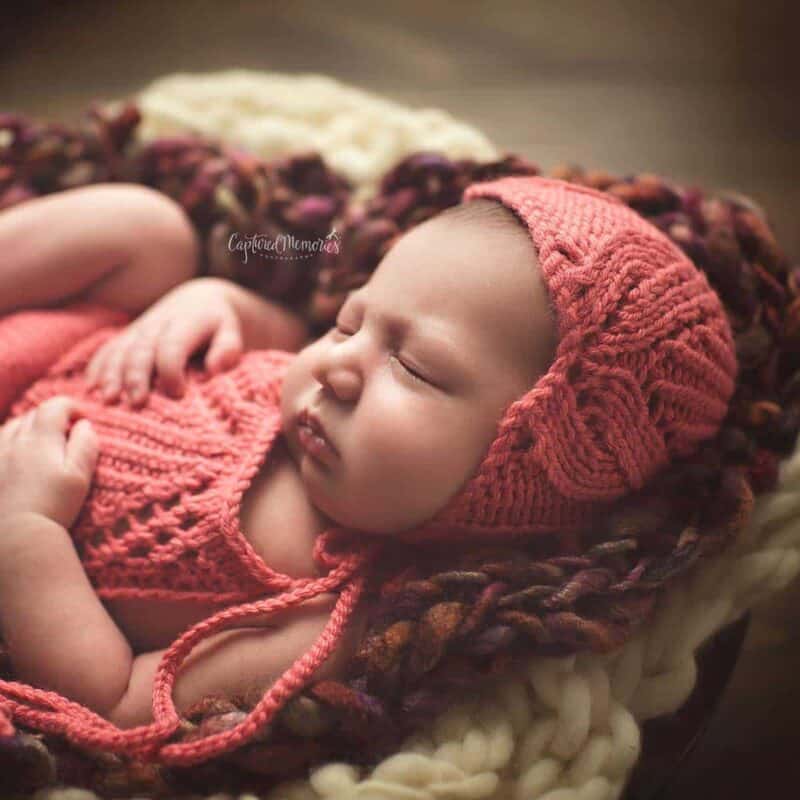 A baby sleeping in a crocheted hat with a tulip pattern.