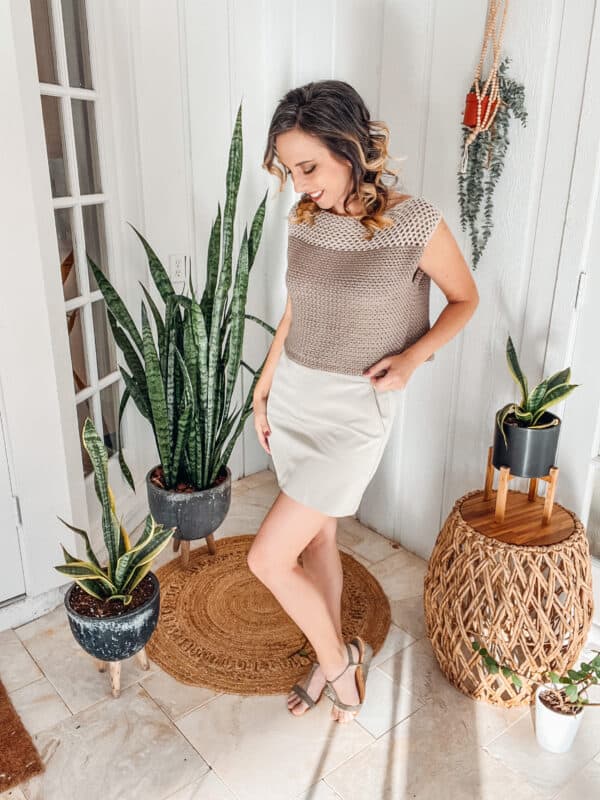 A woman in a tan sweater standing in front of a potted plant.