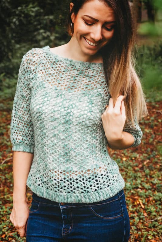 Woman in a crochet summer top smiling outdoors.