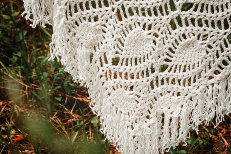 A boho-inspired white crocheted poncho gracefully draped on the grass.
