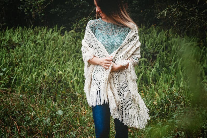 A boho woman donning a crochet wrap in the woods.