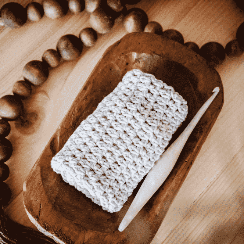 a rolled up yarn washcloth in a wood tray with a crochet hook and decorative beads