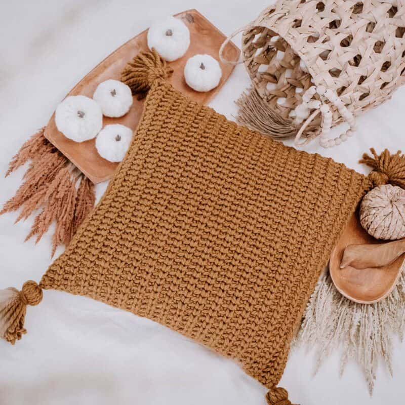 A knitted pillow with tassels and a basket.