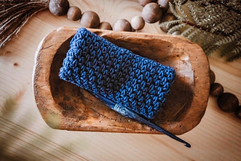 a crochet washcloth sitting in a wood bowl with beads and greenery