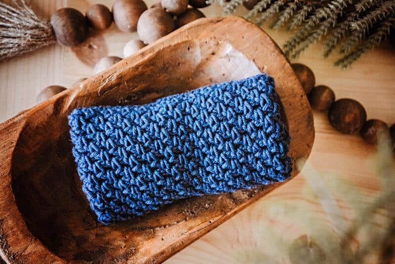 a crochet washcloth sitting in a wood bowl with beads and greenery