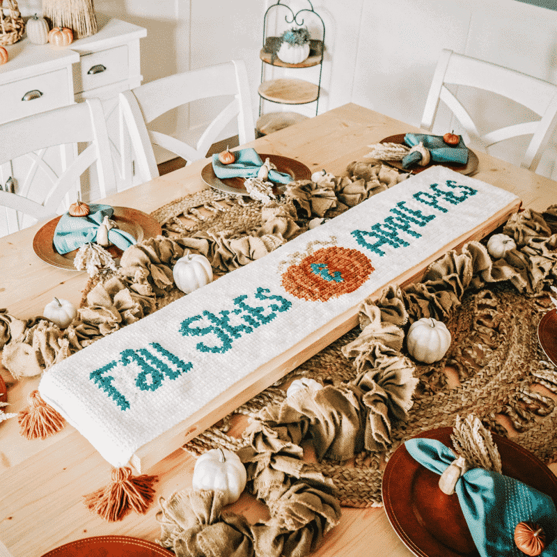 A table adorned with a crochet table runner and pumpkins.