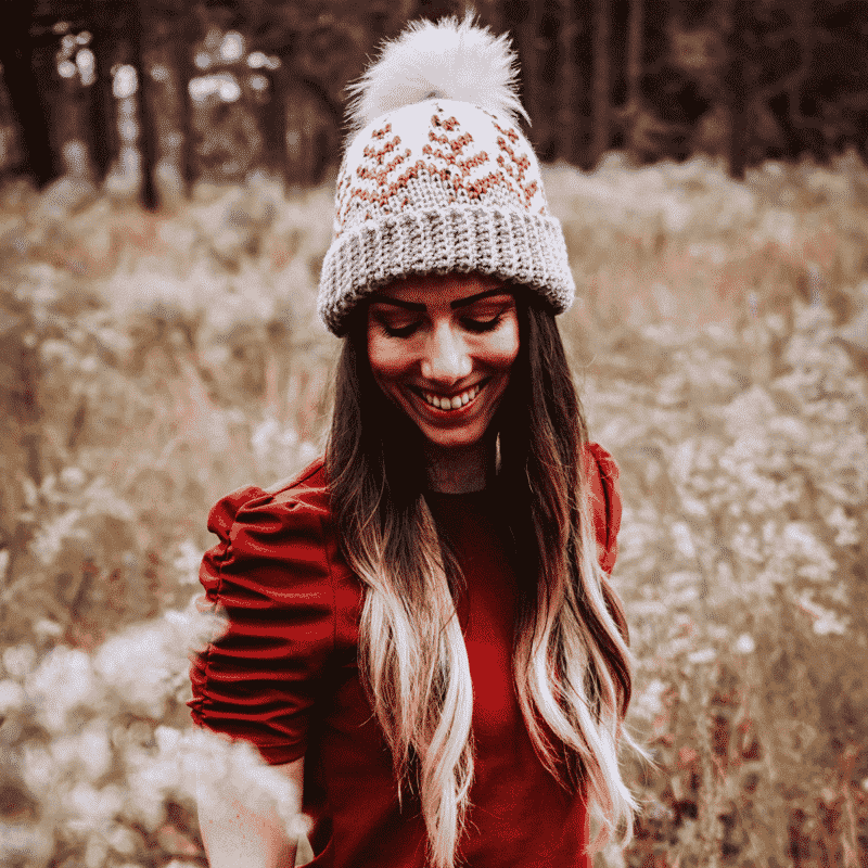 A woman in a red dress smiling in a field adorned with a crochet hat.