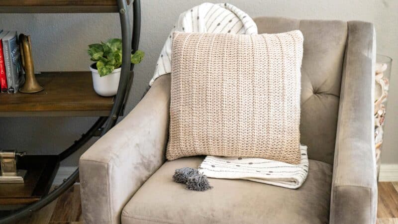 A chair in a living room with a knitted nutmeg pillow.