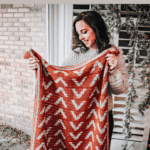 A woman holds up a red and white Arrow Crochet Blanket with an arrow pattern. Text reads "Free Tapestry Crochet Pattern Arrow Blanket" and "www.brianakdesigns.com".