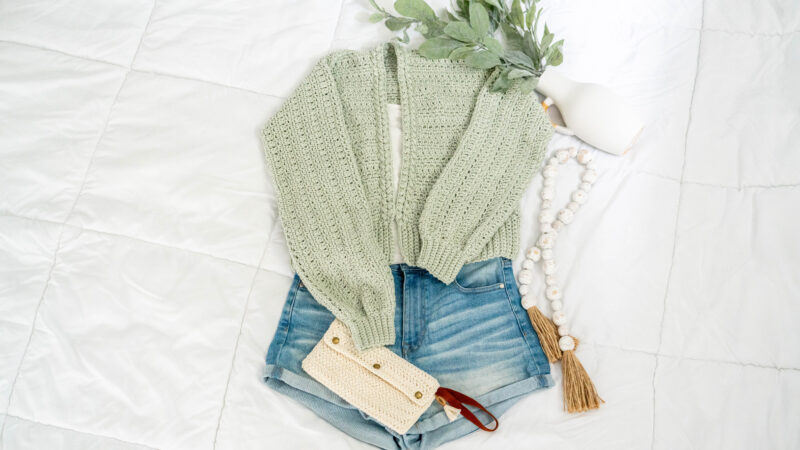 Denim shorts and a green sweater laid on a bed, creating a cozy and relaxed atmosphere.