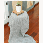A light gray crocheted blanket is draped over a stool with a small potted plant on top. Text reads "Crochet Garden Blanket Free Pattern – How to Crochet Garden Picnic Blanket.