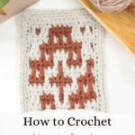 A swatch of mosaic crochet in cream and rust yarn lies on a white surface beside a ball of yarn, wooden tray, and green plant. Text: Learn how to master Mosaic Crochet.