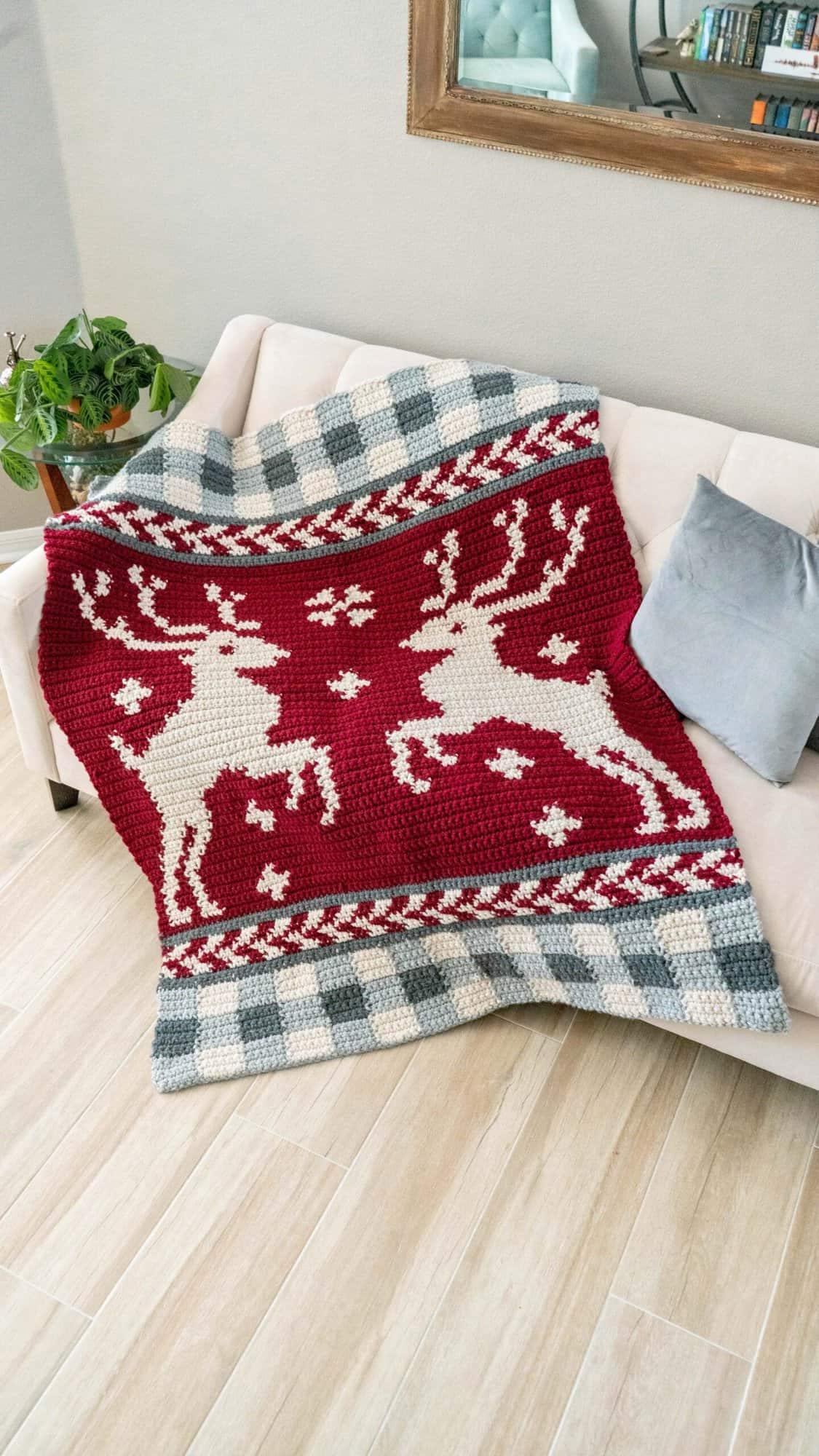 A couch with a crocheted reindeer Prancing Through the Holidays blanket on it.