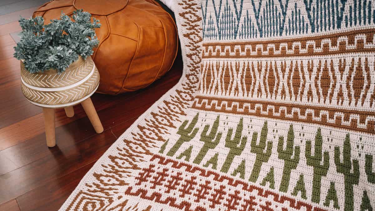 A crochet blanket with a cactus design on it placed on a wooden floor.