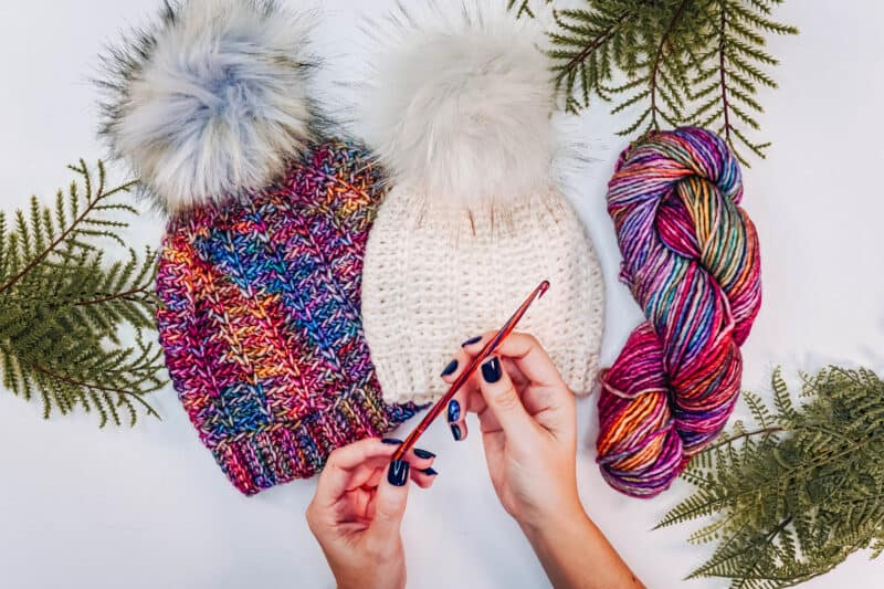 A person crafting a Juniper Knit-Look Crochet Hat with yarn and pom poms.