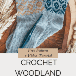 Two Woodland Walker Crochet Socks in earthy tones with patterned cuffs are displayed on a wooden surface, alongside a crochet hook and dried plants, promoting a free pattern and video tutorial.