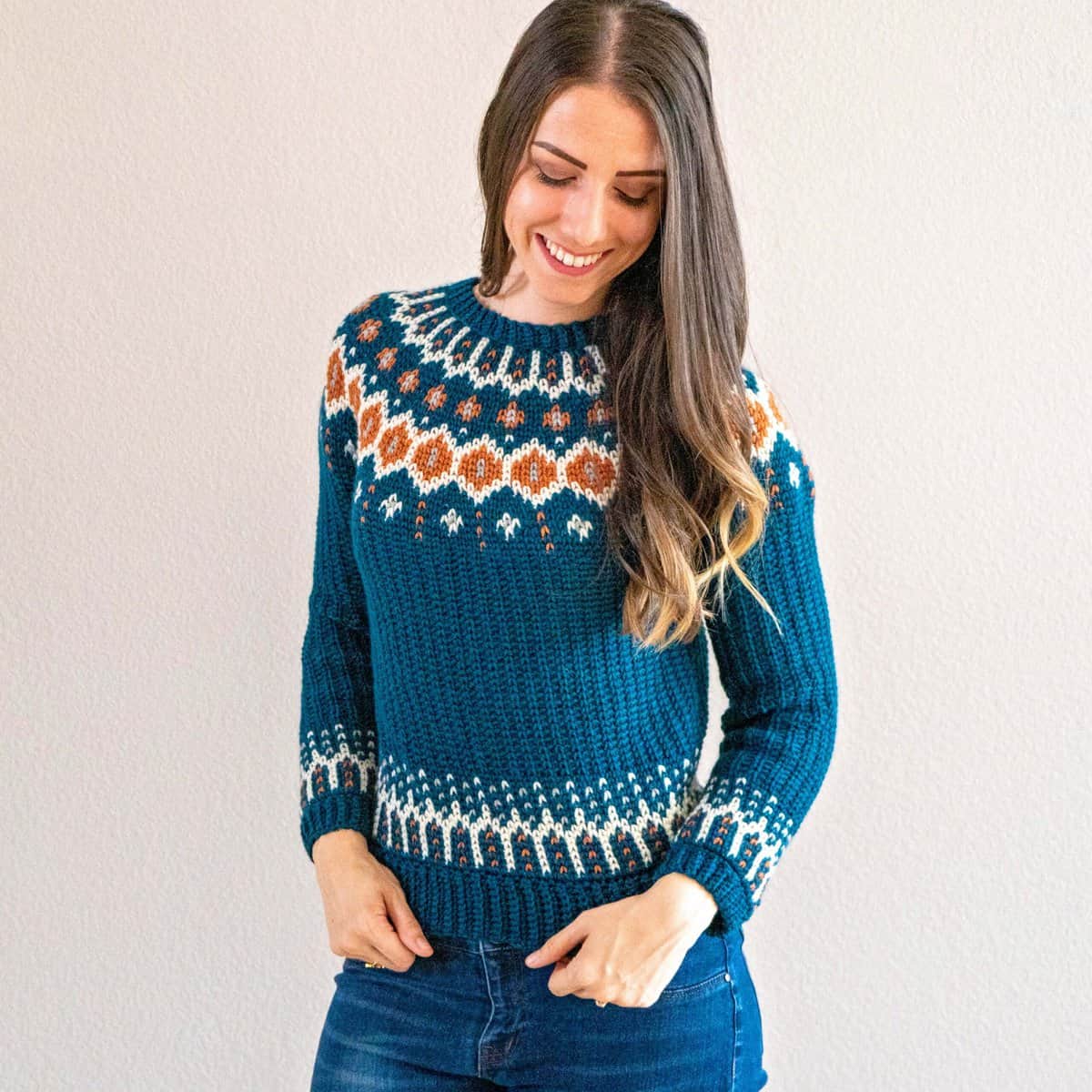 A woman wearing an easy crochet teal sweater and jeans.