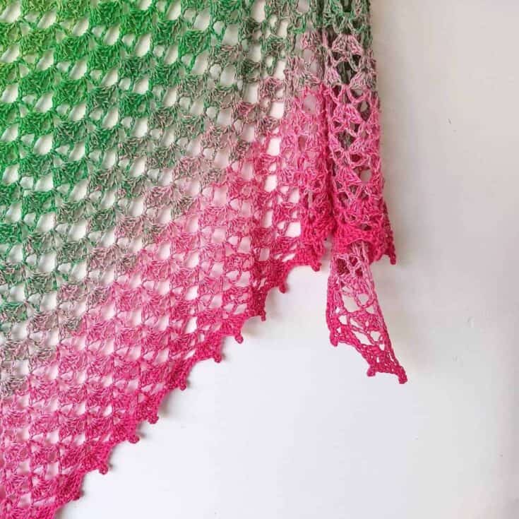 A green and pink crocheted shawl hanging on a wall.