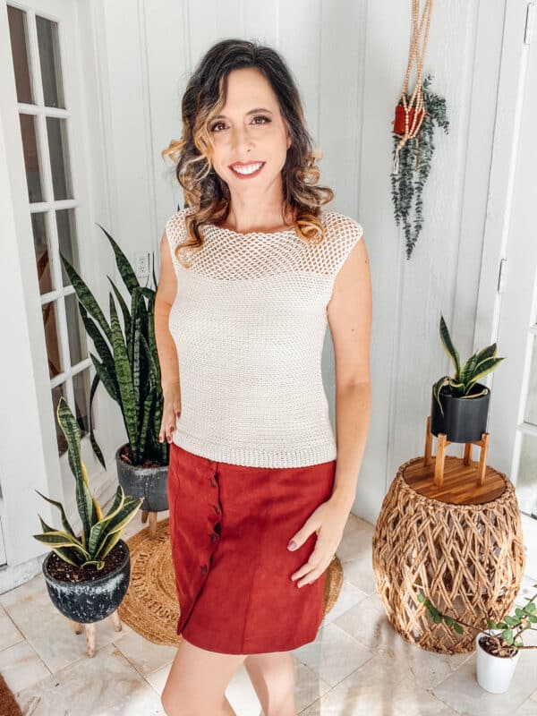 A woman in a *crochet* top standing in front of a potted plant.