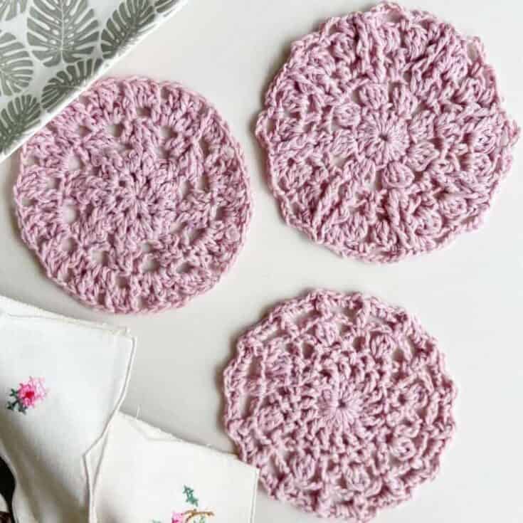 Three pink crocheted coasters on a white table.
