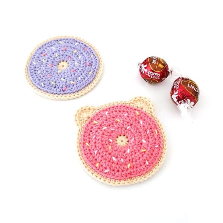 Two crocheted donut coasters next to a candy.