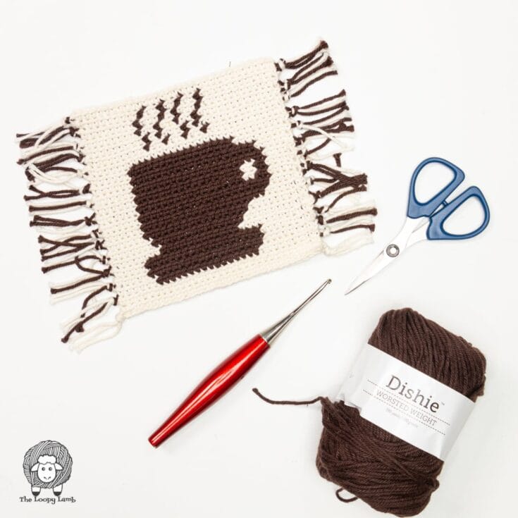 A crocheted coffee cup with scissors and yarn.