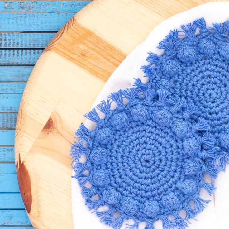 Two blue crocheted coasters on a wooden table.