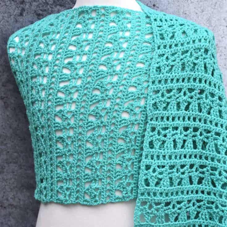 A turquoise crocheted shawl on a mannequin.
