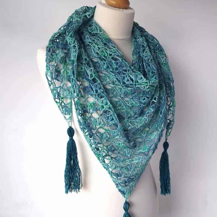A blue and green crocheted shawl with tassels.