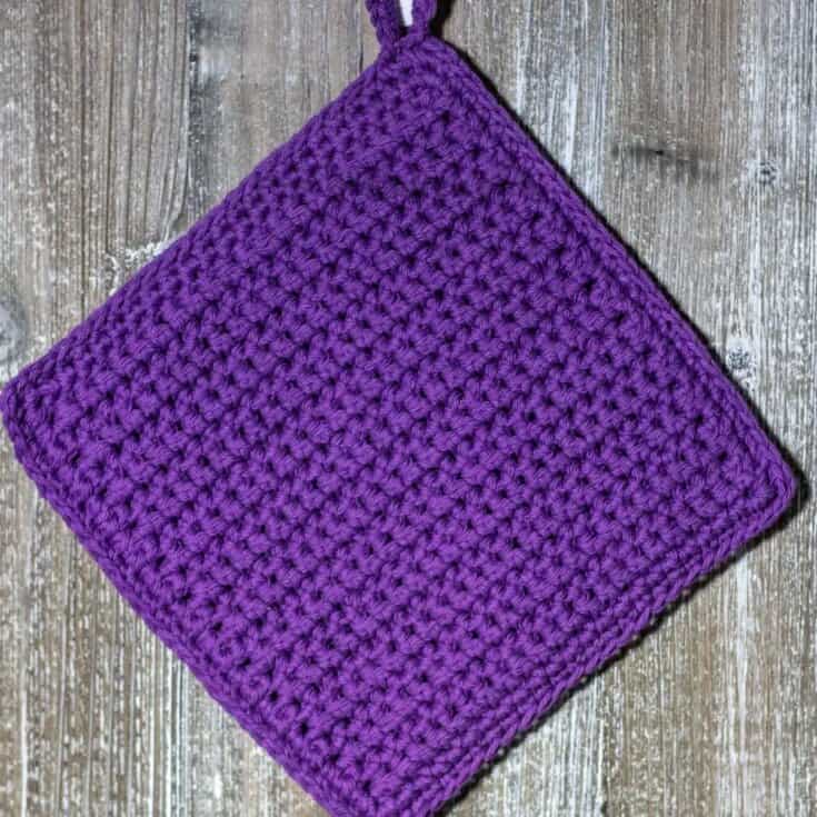 A purple crocheted pot holder on a wooden table.